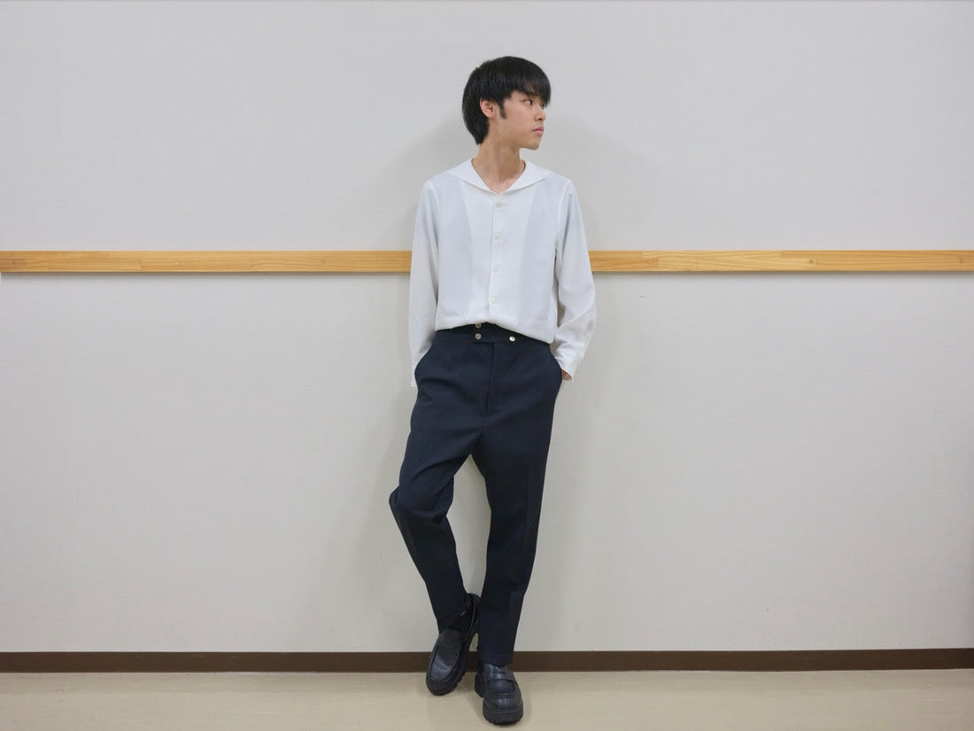 セーラーカラーのシャツを着て、フロントに金属ボタンをあしらったスラックスを履いた男性