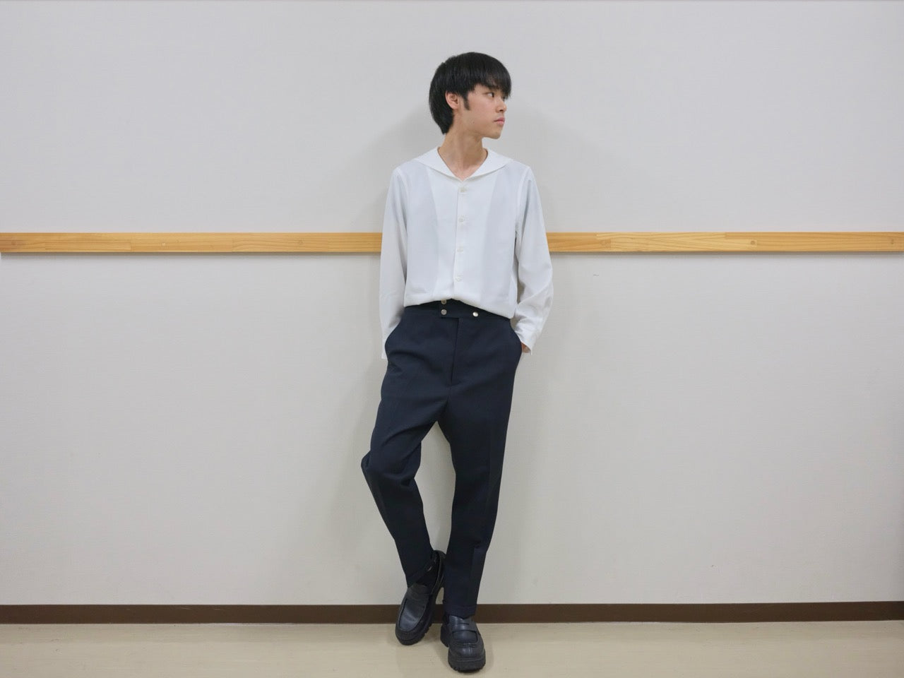 セーラーカラーのシャツを着て、フロントに金属ボタンをあしらったスラックスを履いた男性