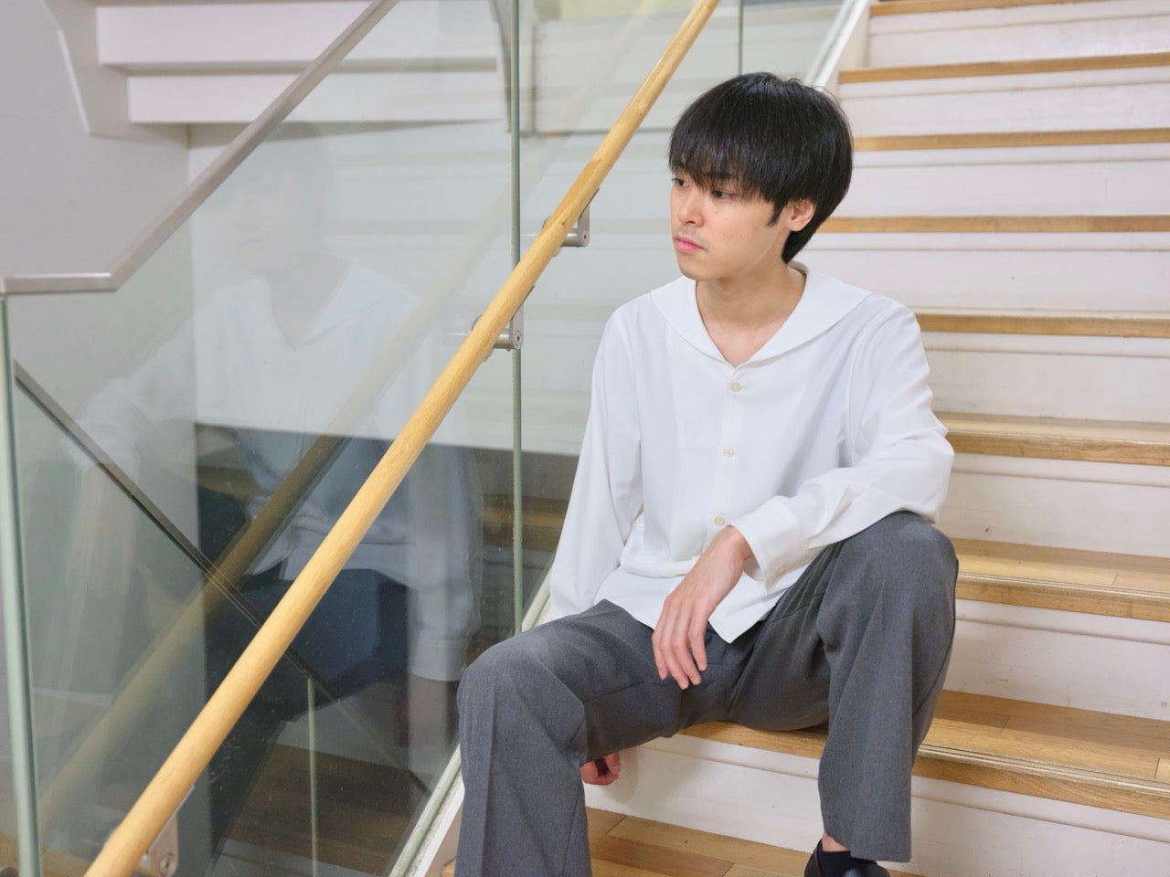 階段に座り、白いセーラーカラーシャツとグレーのパンツを着用した男性モデル