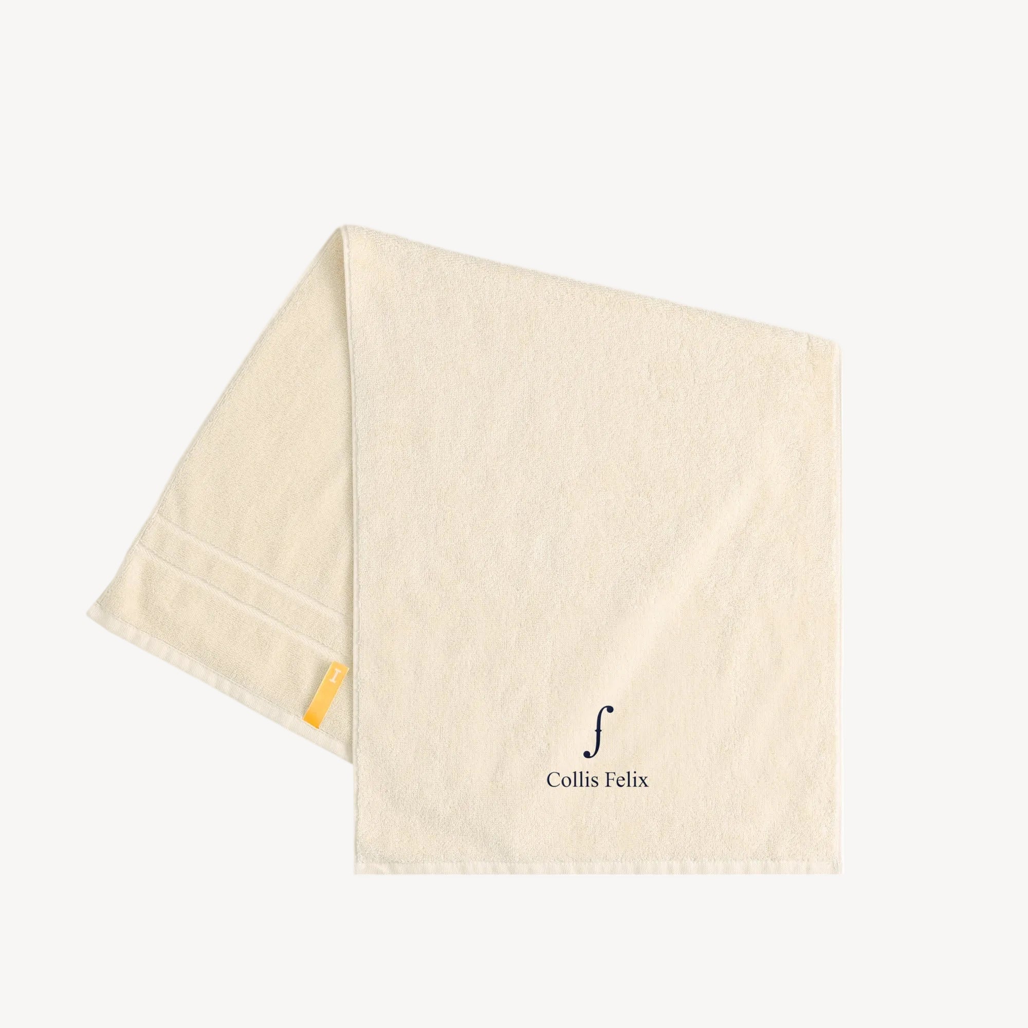 Collis Felixのアイボリーのタオル。下部にブランドロゴが入り、左側にイエローのタグが付いている。