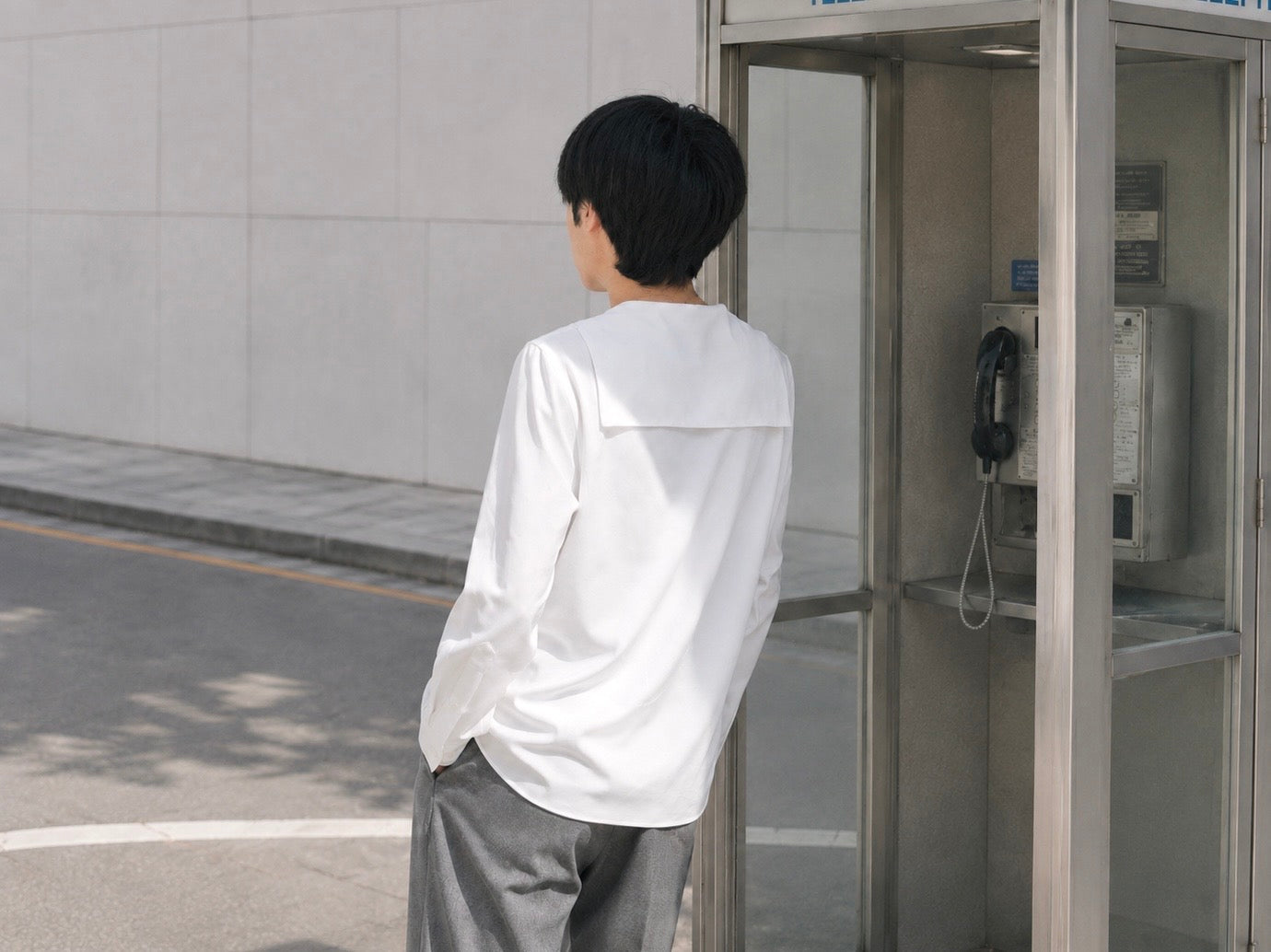 白いセーラーカラーシャツの後ろ姿と街角の電話ボックス