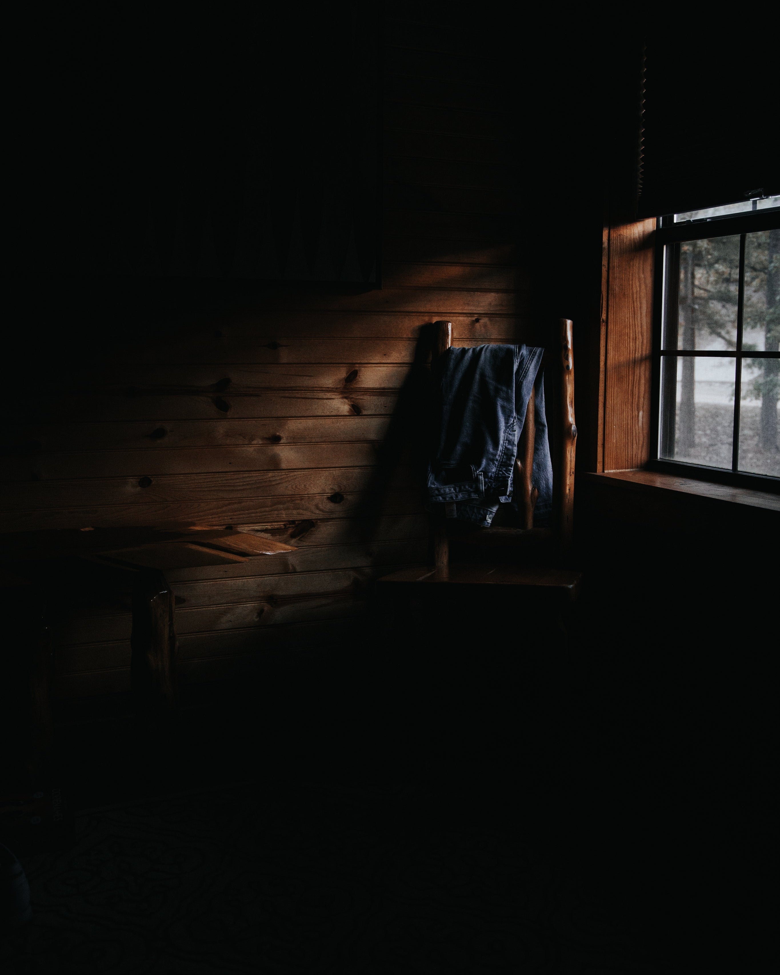 窓から差し込む光が木の壁と椅子に掛けられた服を照らす、静かな山小屋の室内